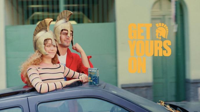 two people hanging out of the roof of a car while wearing roman helmets. they are smiling and looking towards the camera