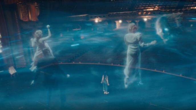 back view of a person standing on a stage as ghosts and a skull surround her