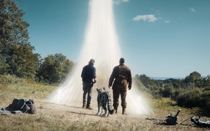 Two men and a snow leopard stand before a bright white portal, reaching up into the sky