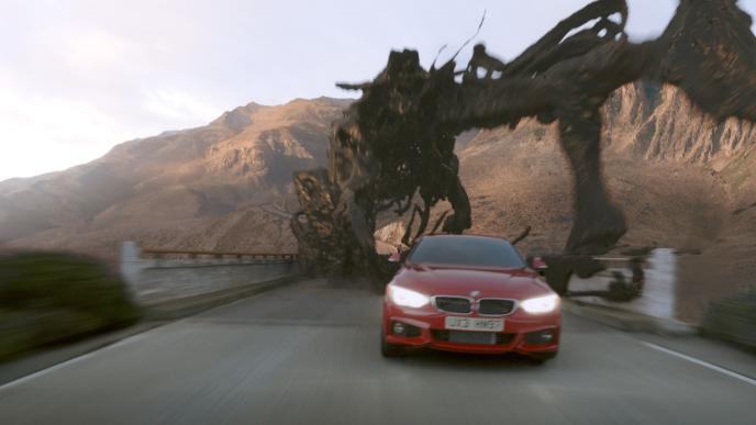 A red car drives down a mountain road at sunset, chased by an alien creature