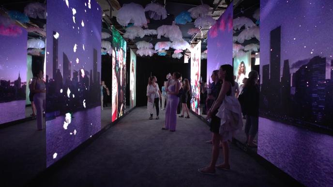 A group of people enjoy the Carrie's Closet experience as they look at different screens featuring iconic looks from 'Sex and the City'