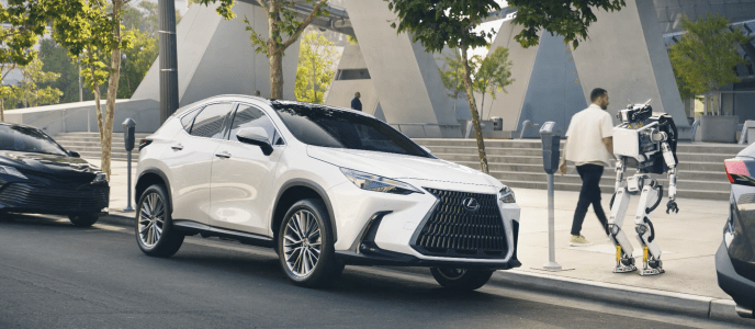 a white Lexus suv parked outside of a building in LA. A man walks out of the vehicle as a robot stands and watches