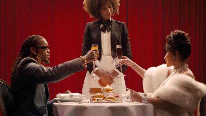 Cardi B and Offset dressed up in nice clothing at a nice restaurant where they are served McDonald's food