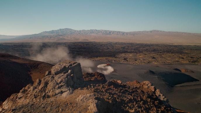 An orange Tayota Tacoma drives through a rocky desert