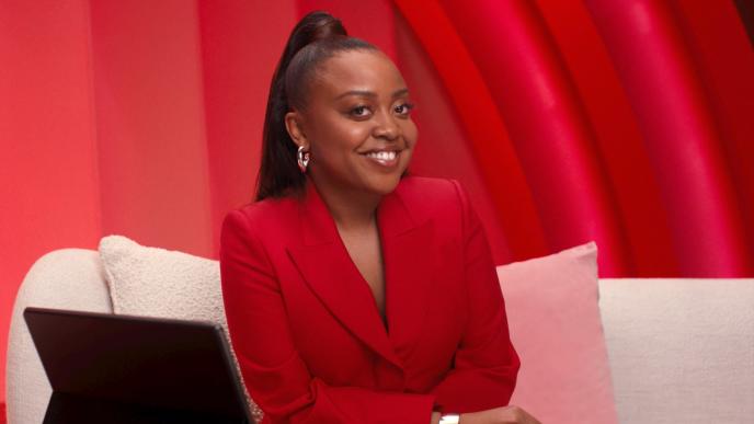 Quinta Brunson in a red blazer sitting on a couch