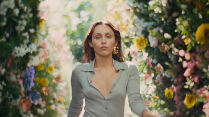 Miley Cyris walks through hedges filled with colorful flowers