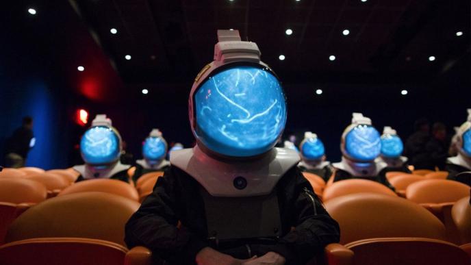 A theatre full of people wearing space helmets that show a VFX blue glowing interior.