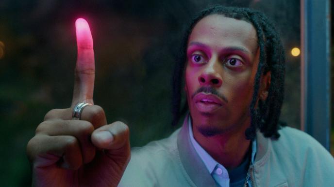 A man holds up his index finger which is glowing pink