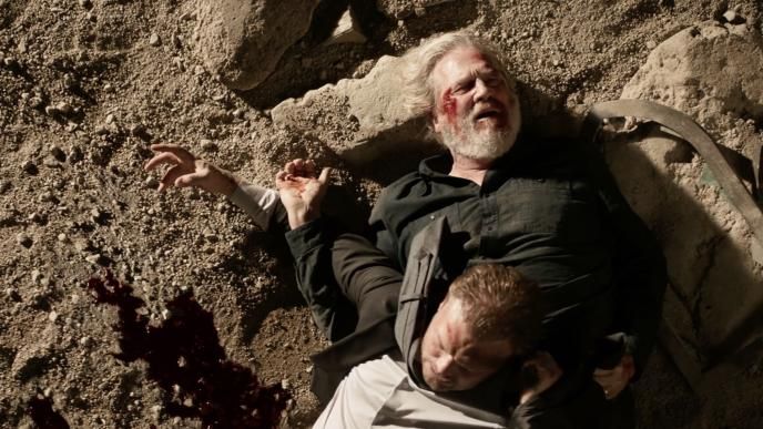 Two men lay on the ground, both bloodied and injured