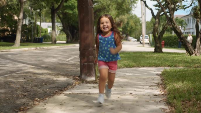 A little girl smiles as she runs through a neighborhood