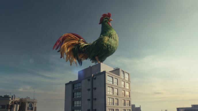 A photo-realistic CGI cockerel crowing on top of an apartment building against a blue sky.