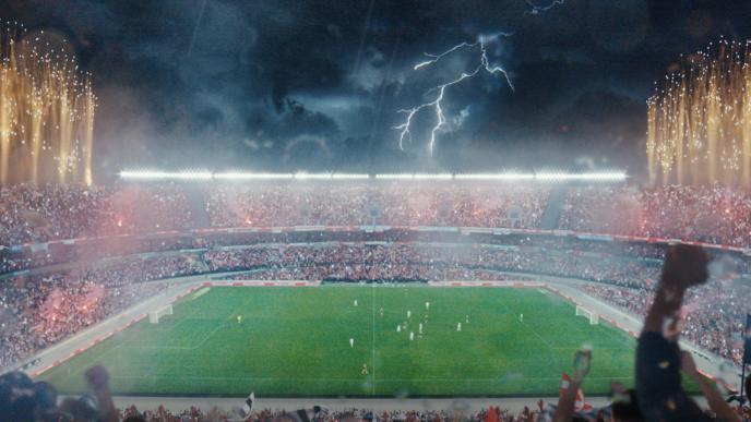 A soccer/football stadium is packed with a large crowd (which has been made by VFX Crowd Simulation). Lighting is striking in the sky