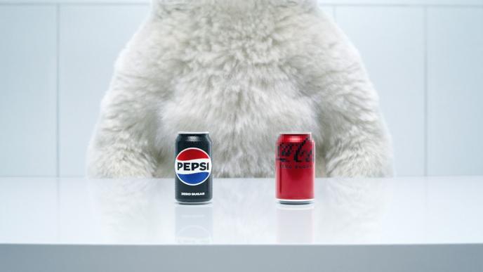 A CG animated polar bear seen from the neck to waist, sitting at a table. In front of the polar bear are two soda cans