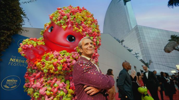 Andy Cohen poses on a red carpet with the CG animated Nerds Gummy Cluster mascot