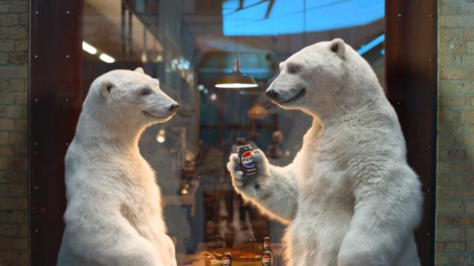Two CG animated polar bears face each other, one offering a Pepsi can, through a café window with people behind.