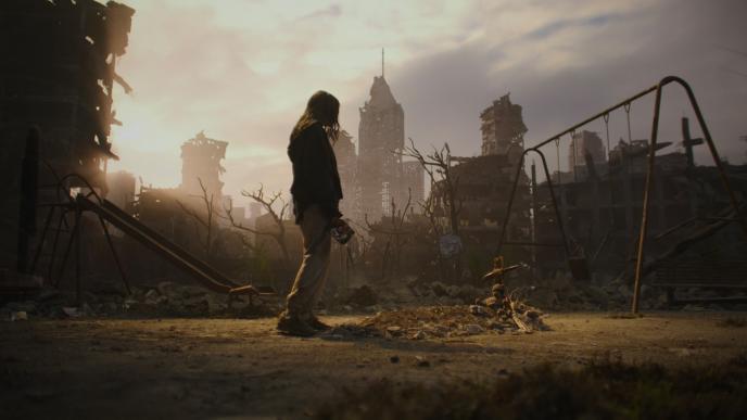 Silhouetted woman stands in desolate devastated playground, facing makeshift teddy bear memorial amid crumbling skyscrapers and barren trees at sunset.
