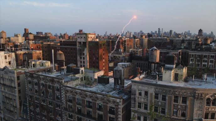 City rooftops and water towers at dusk as a glowing flare streaks into the sky above the distant skyline.