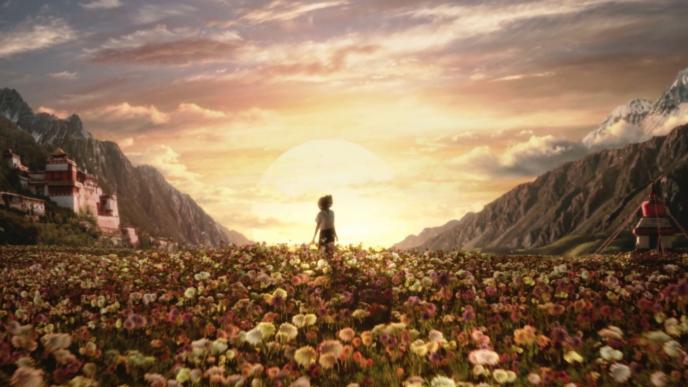 a person standing in the centre of a flower field in front of a sunset. there are mountains and houses on each side