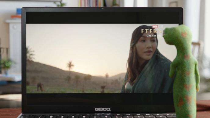 back shot of animated geico mascot watching a the marvel eternals film on a geico laptop