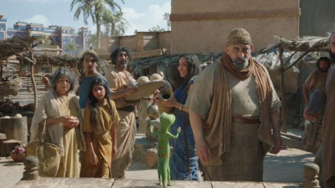 back shot of geico mascot talking to a group of people in a desert city