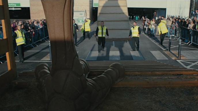 people in high visibility jackets look on as they are engulfed by the shadow of a giant chocolate hens leg