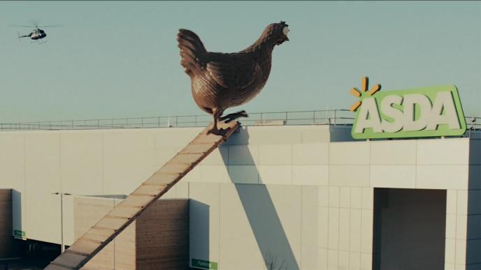 a giant chocolate hen walking up the side of an asda building as a helicopter flies nearby