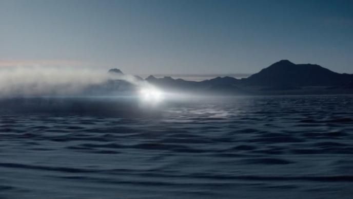 a mountainous desert terrain with a car and its headlights brightly shining in the centre of the shot