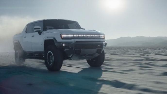 front shot of the gmc hummer ev pick up truck driving on terrain with the sun gleaming in the background
