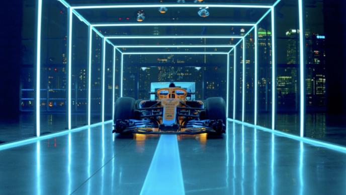 a race car inside of a transparent room that is layered in blue neon lights. the nighttime city skyline twinkles in the background