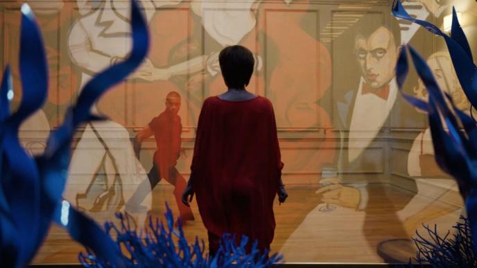 back shot of a person looking at a translucent collage of someone interpretative dancing and paintings that are covering the entire screen
