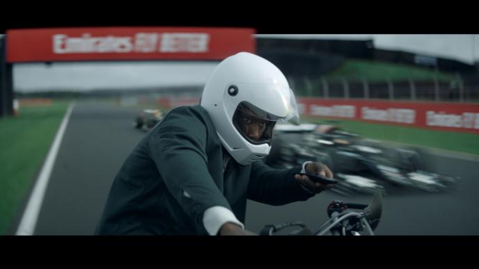a person in a helmet sitting on a motorcycle while holding up a tv remote. they are on a formula one race car track