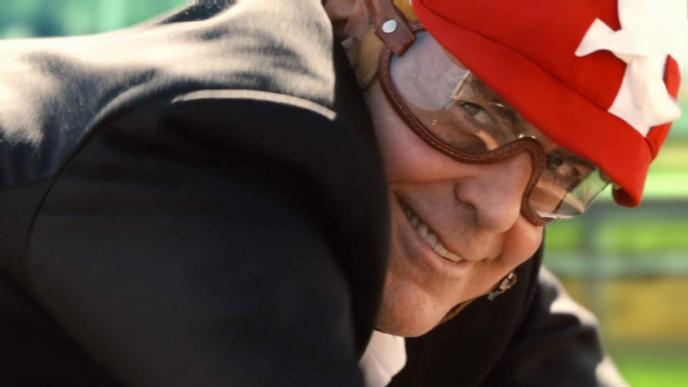 close up shot of actor george clooney's face. he is looking into the camera as he smiles. he is wearing motorcycle goggles and a hat