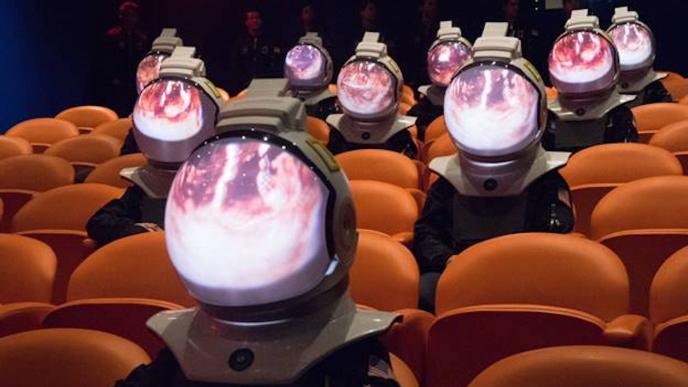 cinema audience of people in space suits with nebula visuals on their helmets sitting in orange seats