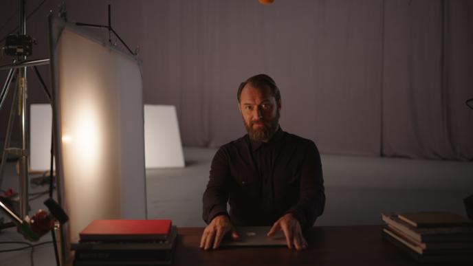 actor jude law sitting at a desk in a dimly lit film studio