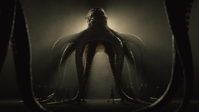 a dimly lit, giant animation of an octopus. there are people standing under it. one person is walking in the centre