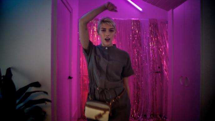 a person holding up their arm mid singing in front of a pink background