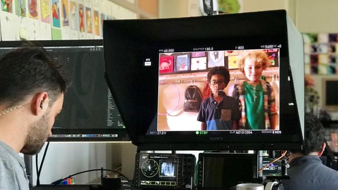 behind the scenes perspective of a cameraman and camera screen with two children side by side on the screen