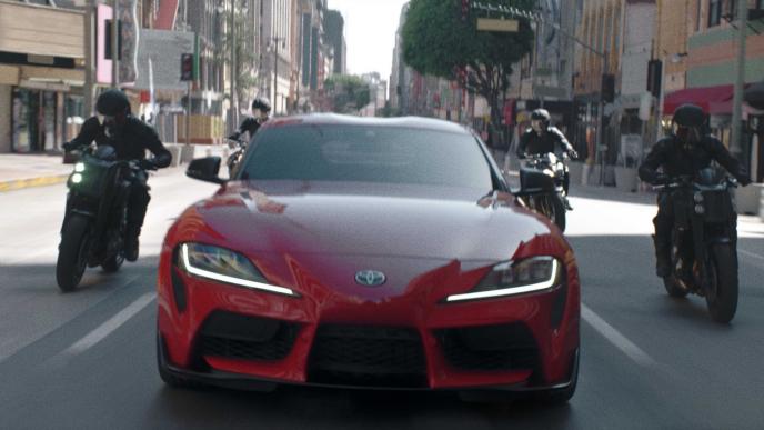 front shot of a red toyota car that is followed by four motorcycles