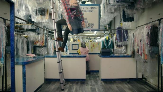 a person in a dry cleaners coming down a ladder while holding a human suit