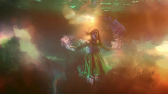 a person floating with their arms open looking around in awe. they are underwater and there is colourful hazy smoke surrounding the environment