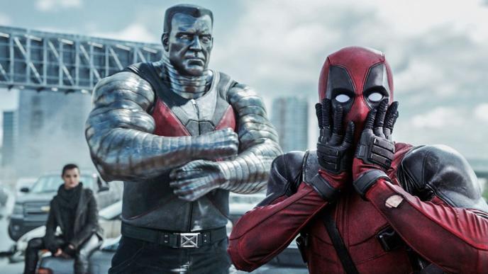 deadpool looking at the camera shocked with his hands on his face as colossus is standing with his arms crossed in the back