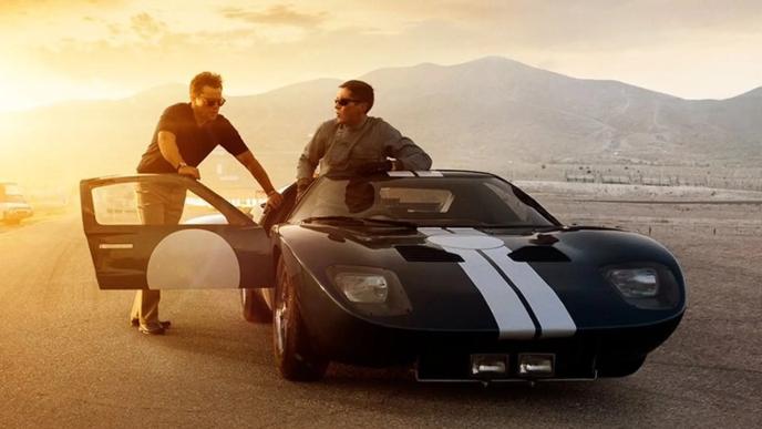 poster of two men standing outside of a ferrari car as the sun sets in the background