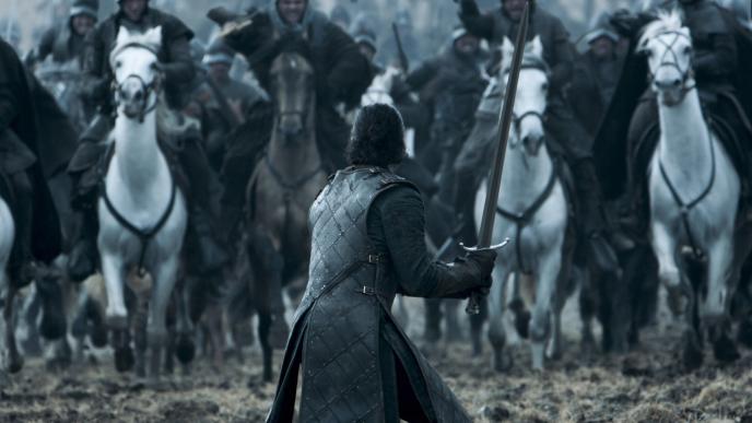 back view of jon snow holding a sword facing soldiers on horses