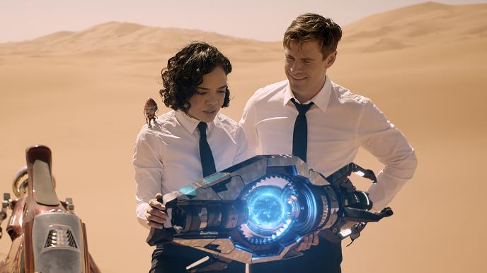 actress tessa thompson as molly and actor chris hemsworth wearing white shirts and black ties holding a time machine in a desert