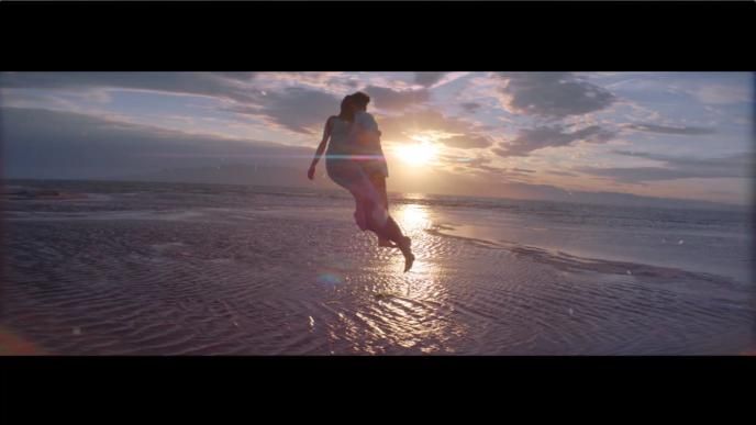 a couple floating in air in front of a sunset by the sea