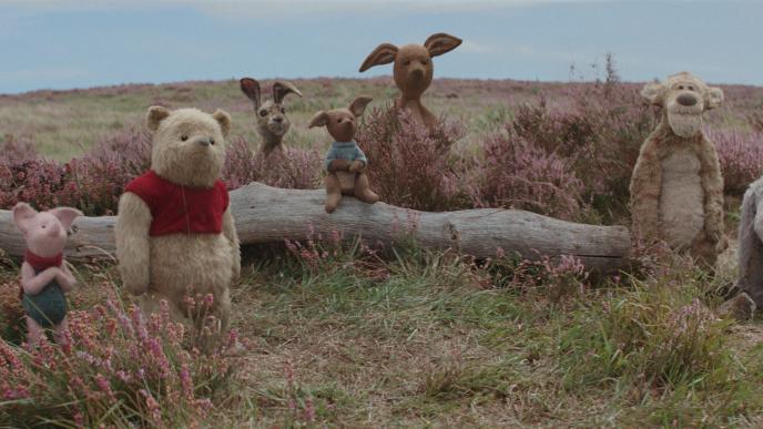 cg animated photorealistic winnie the pooh characters standing together in between a tree log in a field. from the left to the right is piglet, winnie the pooh, rabbit, roo, kanga, tigger and eeyore