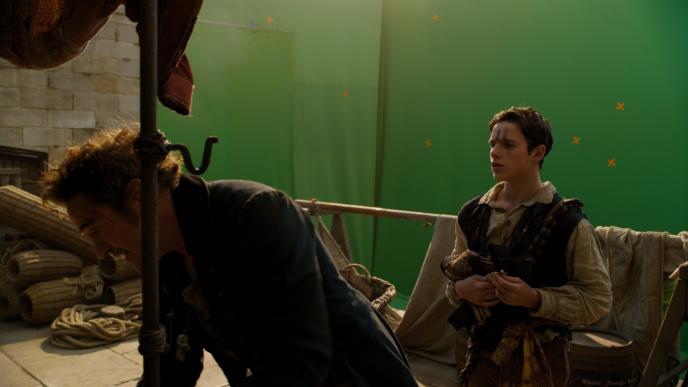 actor robert downey jr as doctor dolittle crouching and actor harry collett as tommy stubbins standing in front of a green screen