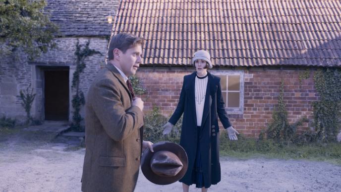 actor standing in front of a brick and stone bungalow