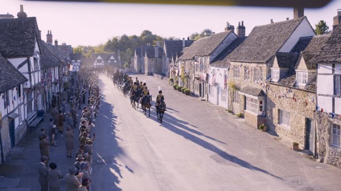 houses lined up on a street as a crowd watch people on horses go by