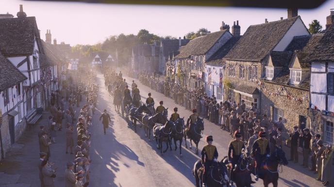 houses lined up on a street as a crowd watch people on horses go by